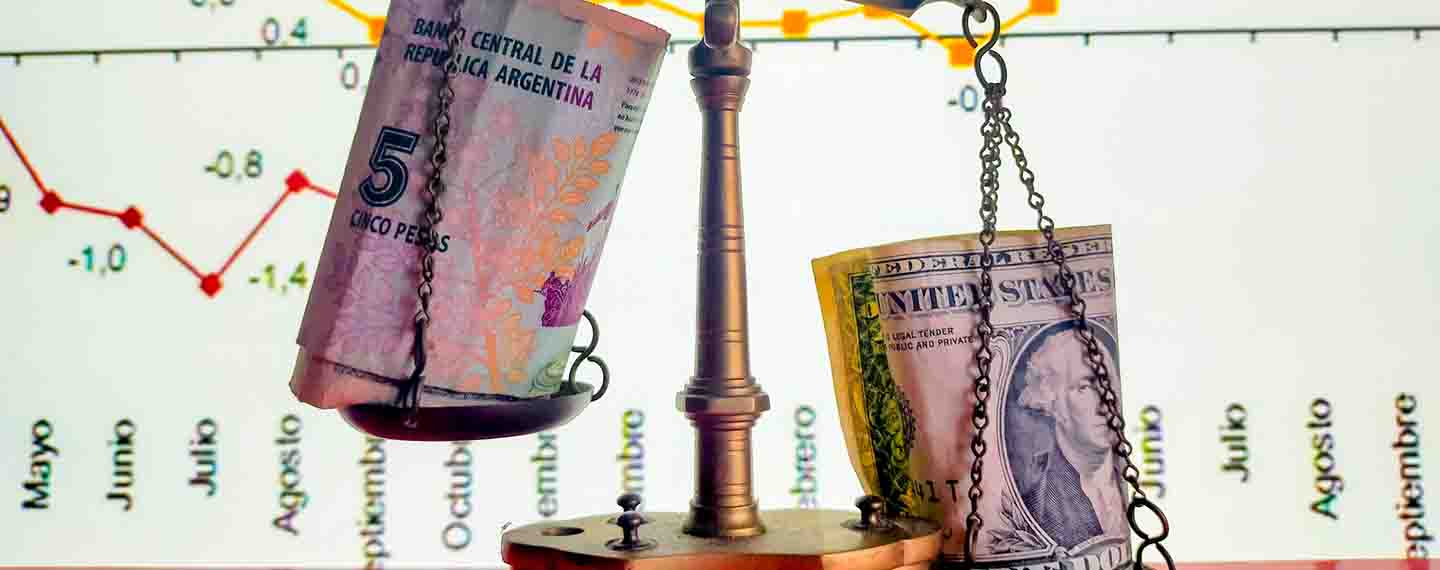 Detail of a balance scale holding Argentine pesos and dollars in their saucers. Background: Screen with timeline of the rise and fall of the stock market.