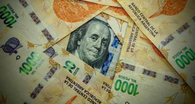 Detail of a green and black 100 US dollar banknote partially visible beneath several orange, violet, and green 1,000 Argentine peso notes. Argentina